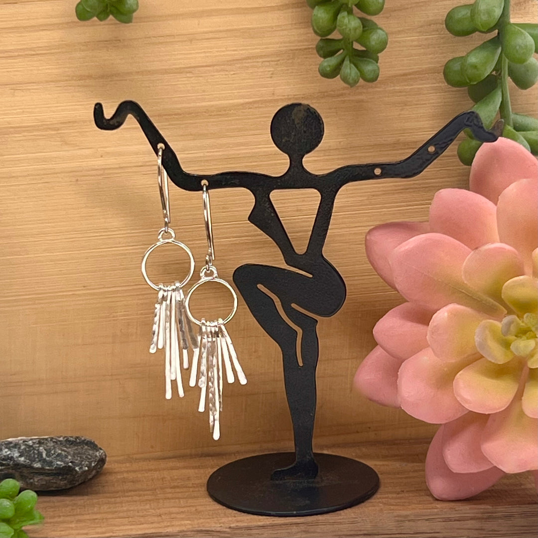 Feather Earrings on lady silhouette on wood block with greenery and pink flower to the side
