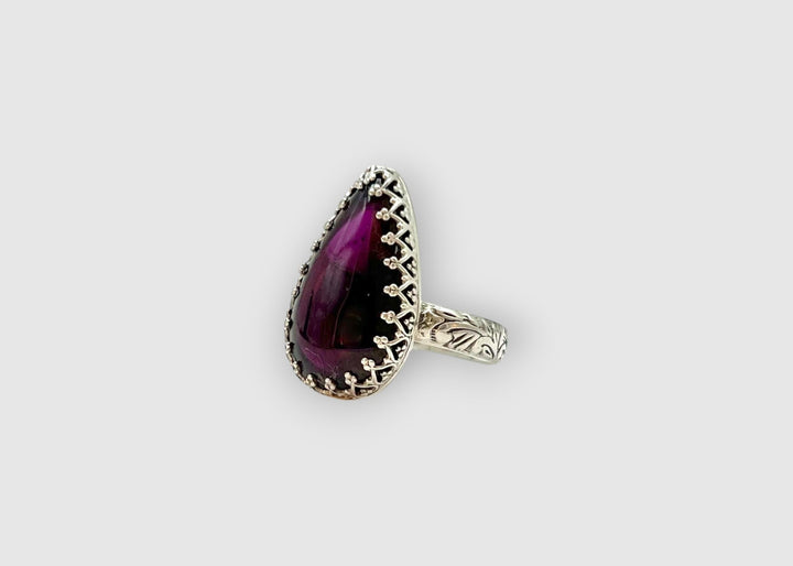 Ring with a purple teardrop-shaped gemstone on a light gray background