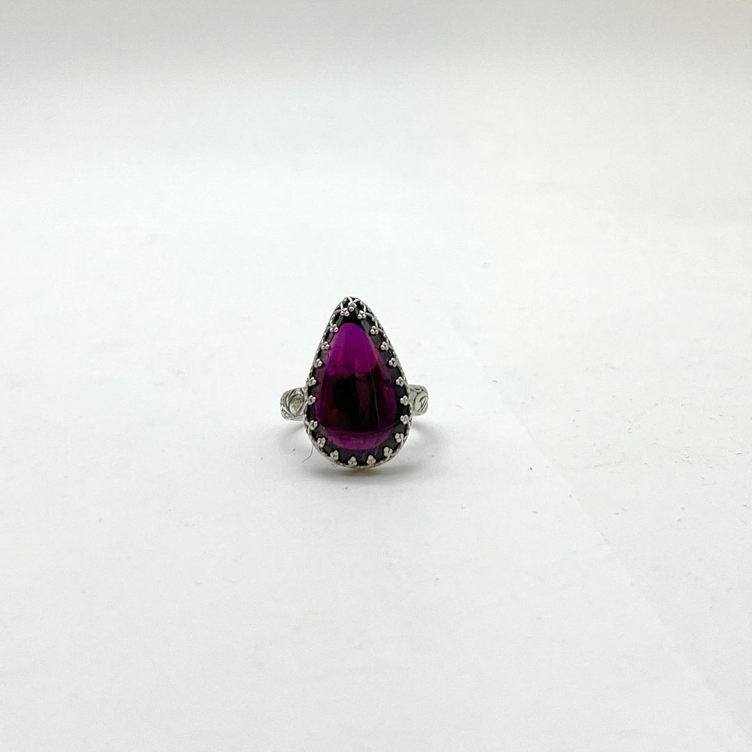 Ring with a purple teardrop-shaped gemstone on a white background
