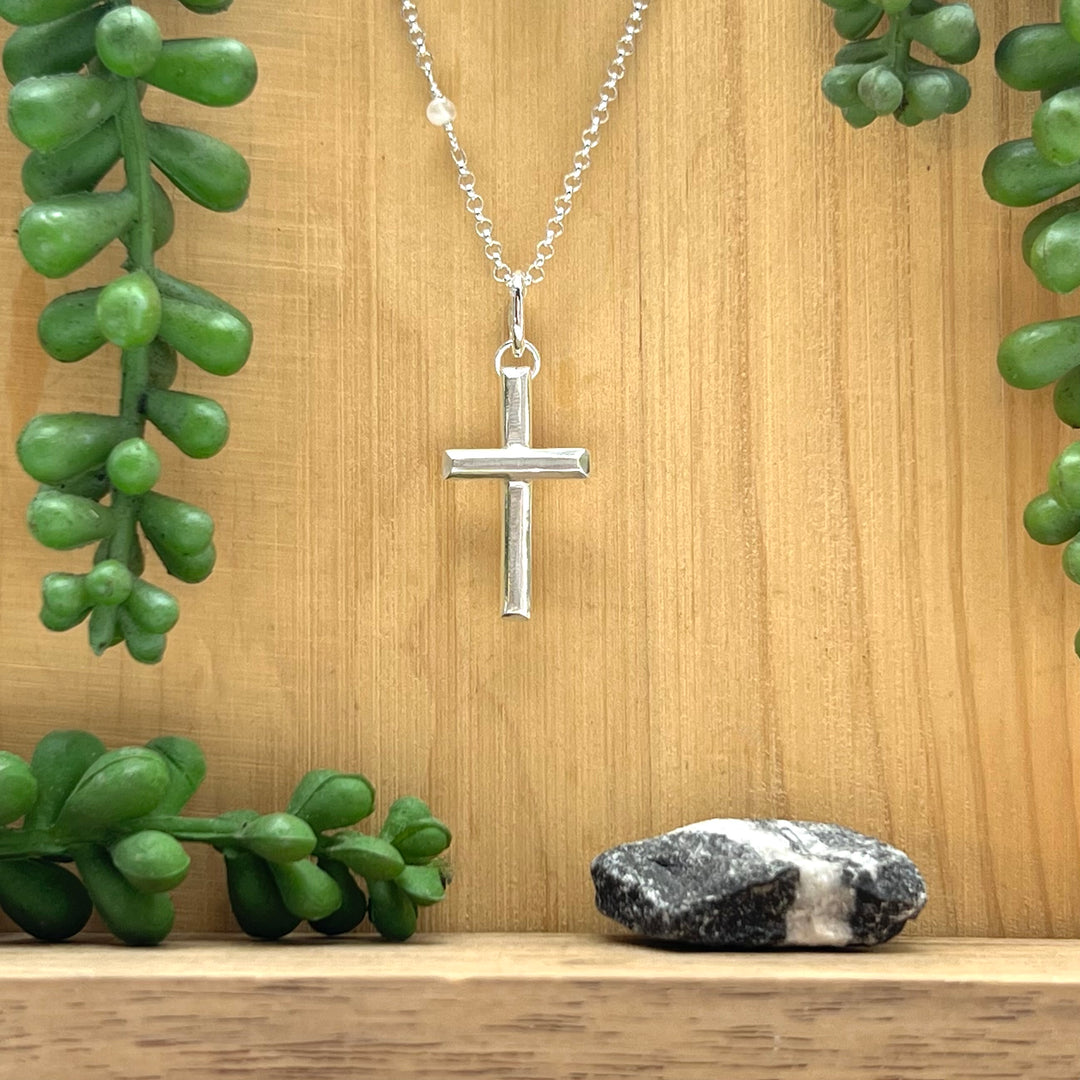 Silver cross necklace on a wooden surface with green plants