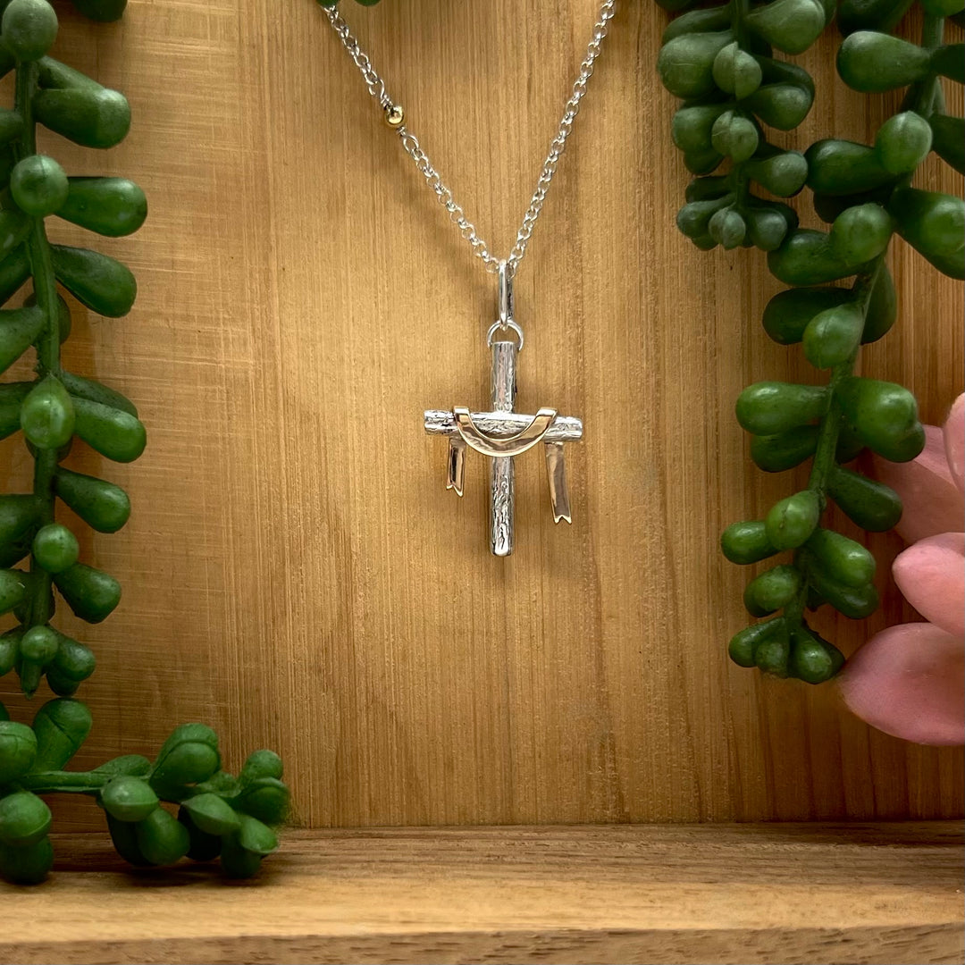 Silver cross pendant necklace on a wooden background with green plants