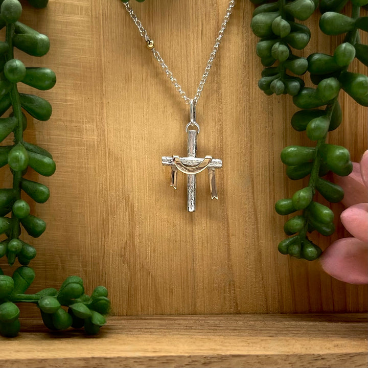 Silver cross pendant necklace on a wooden background with green plants